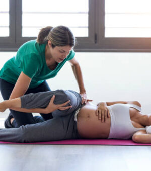 Shot of physiotherapist helping to beautiful pregnant woman for doing pilates exercises preparing for childbirth.